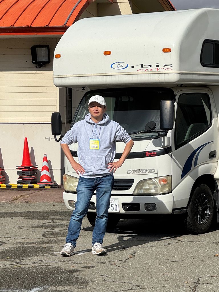 キャンピングカーの前に立つ、ピクセルドライブ株式会社代表取締役 山縣麻人